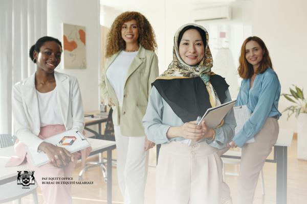 Four professionals standing in a bright office setting, each holding documents or a notebook. A desk, chair, wall art, and a potted plant are visible in the background. In the lower left corner, the Ontario logo and text read: “PAY EQUITY OFFICE BUREAU DE L’ÉQUITÉ SALARIALE Ontario.”